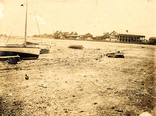 A beach with sailboats on shore and buildings in the background.