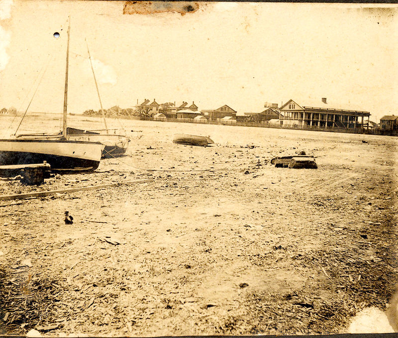 A beach with sailboats on the shore and buildings in the background.