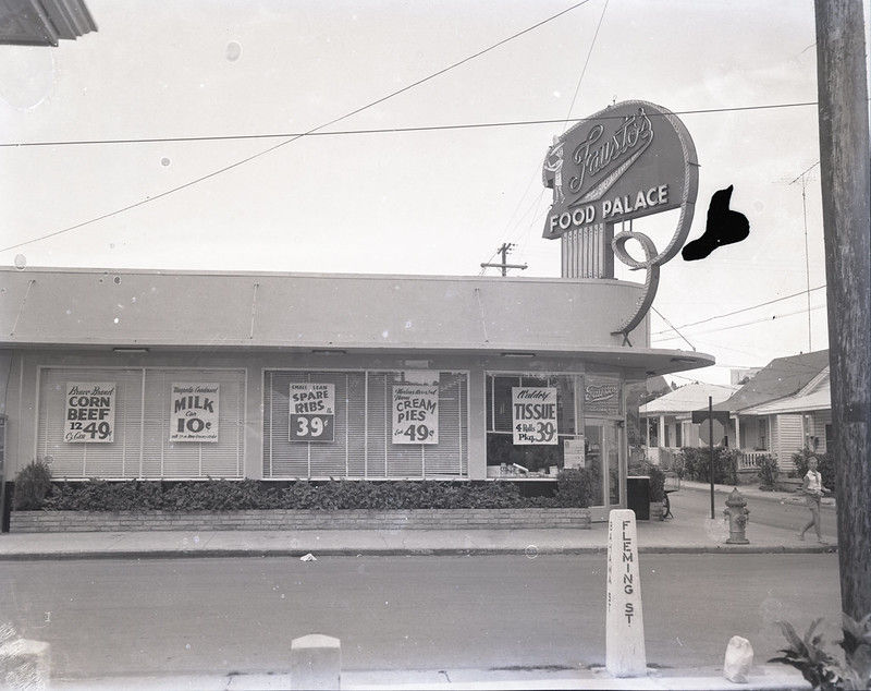 A grocery store with signs offering prices in the window and a sign that reads Fausto's Food Palace.