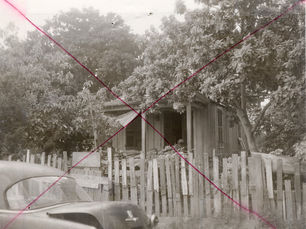 a cottage behind a picket fence. The photo has a red X drawn across it.
