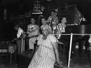 A woman leans on a stage with musicians behind her