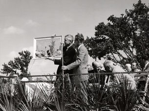 A man at a microphone holds up a framed picture of a coral reef