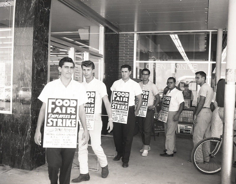 Men on a picket line in front of a store, carrying signs that say Food Fair Employees on Strike.