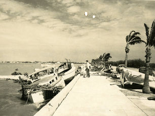 people on a seawall with wrecked boats alongside
