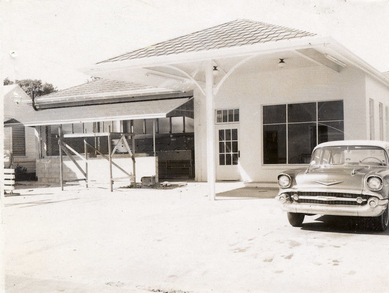 A 1950s stype car parked in front of a service station style building.