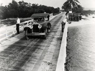 A bridge with two people fishing and a 1920s style car