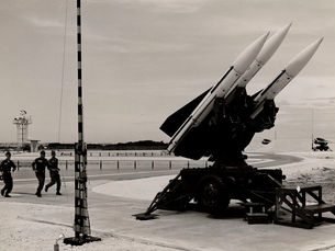 Three people in uniform run past a missile array