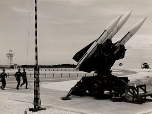 Three people in uniform run past a missile array