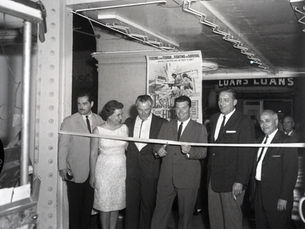 Six people stand in a row behind a ribbon