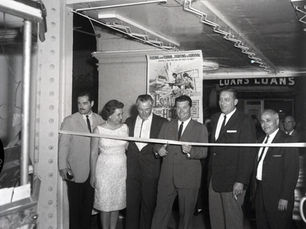 Six people stand in a row behind a ribbon