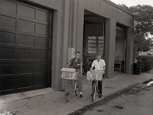 Two people with bicycles with large front baskets outside of a garage