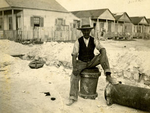 A man sitting on a segment of pipe in front of a row of cottages