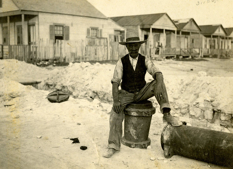 A man sitting on a segment of pipe in front of a row of cottages