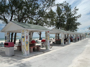 A row of open shelters with colorful paintings on them at a beach.