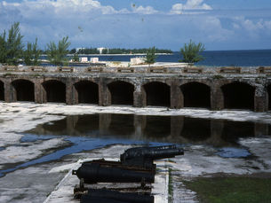 The interior of a fort with water in the background and a large gun in the foreground