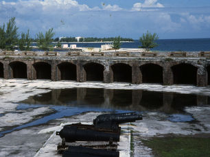 The interior of a fort with water in the background and a large gun in the foreground
