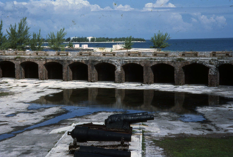 The interior of a fort with water in the background and a large gun in the foreground.