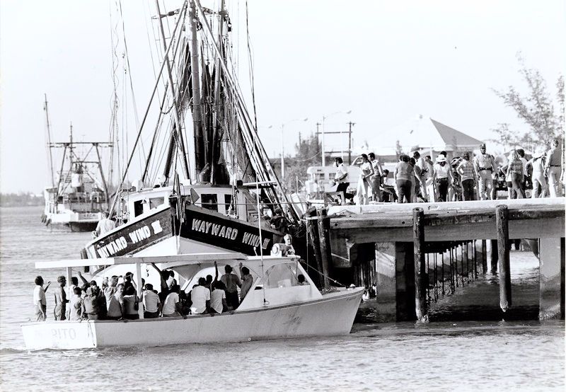 A crwoded boat approaches aa dock with a lot of people on it.