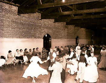 Couples dancing while more people sit in chairs along the wall.