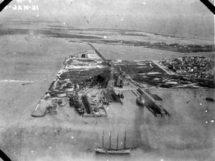 Aerial view of an island connected to other islands by a railroad with a sailing ship in front of it.