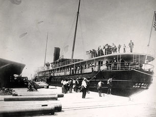 People on and next to a steamship moored at a dock.