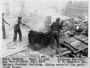 People in an industrial workspace. Text at bottom of photo reads Naval Station Sept. 11, 1941. Contract NOy-4411. Key West, Fllrida 4411-5a-7 W.P. Thurston Co. Battery Overhaul Building. Mixing material for acid-proof floor. 