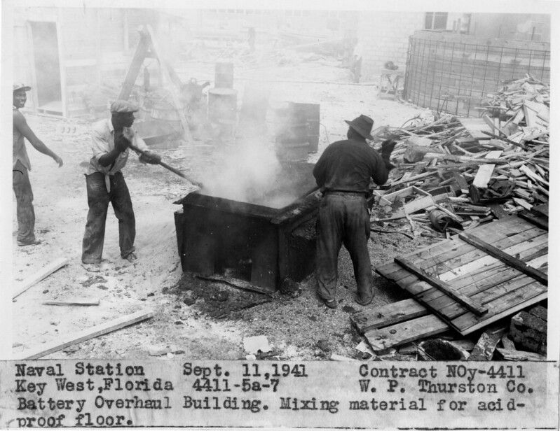 People in an industrial workspace. Text at bottom of photo reads Naval Station Sept. 11, 1941. Contract NOy-4411. Key West, Fllrida 4411-5a-7 W.P. Thurston Co. Battery Overhaul Building. Mixing material for acid-proof floor. 