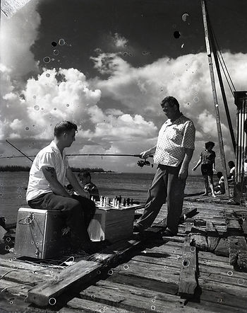 Two men on a dock with fishing poles and a chess board.