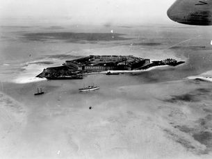 Aerial view of a fort on an island with ships moored nearby.