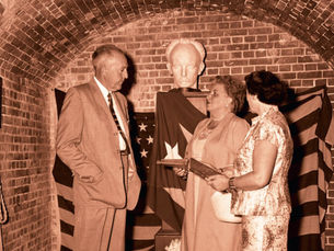 Three people stand in front of a bust in a bricked archway.