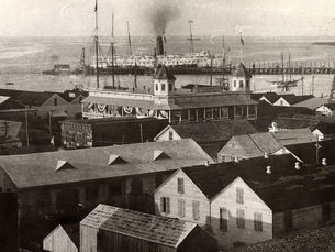 A developed waterfront area with a steamship on the water in the background.