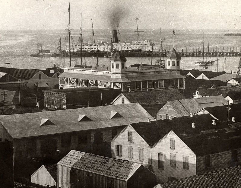 A developed waterfront area with a steamship in the water in the background.