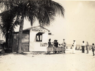 A line of people in front of a small building on a beach.