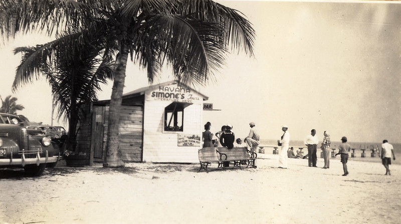 A line of people in front of a small building on a beach.