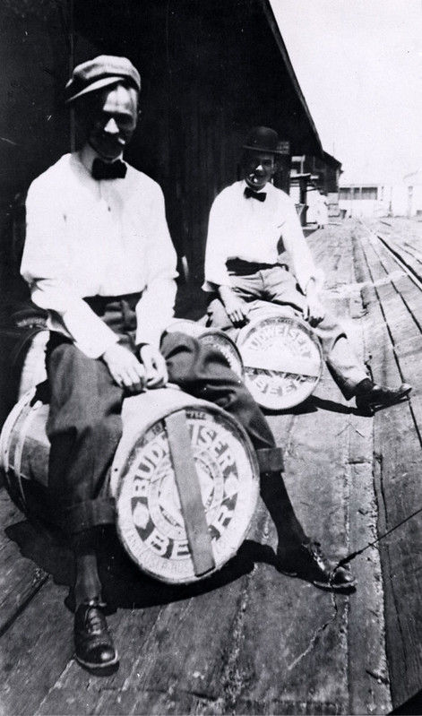Two people on a dock sitting on barrels labeled Budweiser Beer.