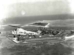 A navy helicopter flying above a brick fort on the water.