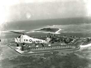 A navy helicopter flying above a brick fort on the water.