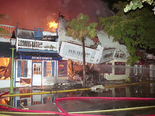 Several buildings on a streetfront on fire, one with a marquee that reads The Copa hanging down.