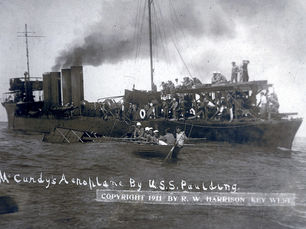 a half sunken airplane near a steamship and a rowboat with sailors. Text on photo reads McCurdy's Aeroplane by USS Paulding. Copyright 1911 by R.W. Harrison.