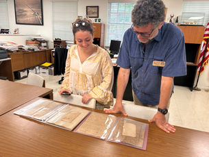 Two people look at documents in plastic sleeves on a table