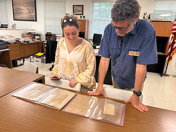 Two people look at documents in plastic sleeves on a table