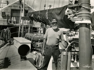 A man stands next to a furled sail on the deck of a sailboat